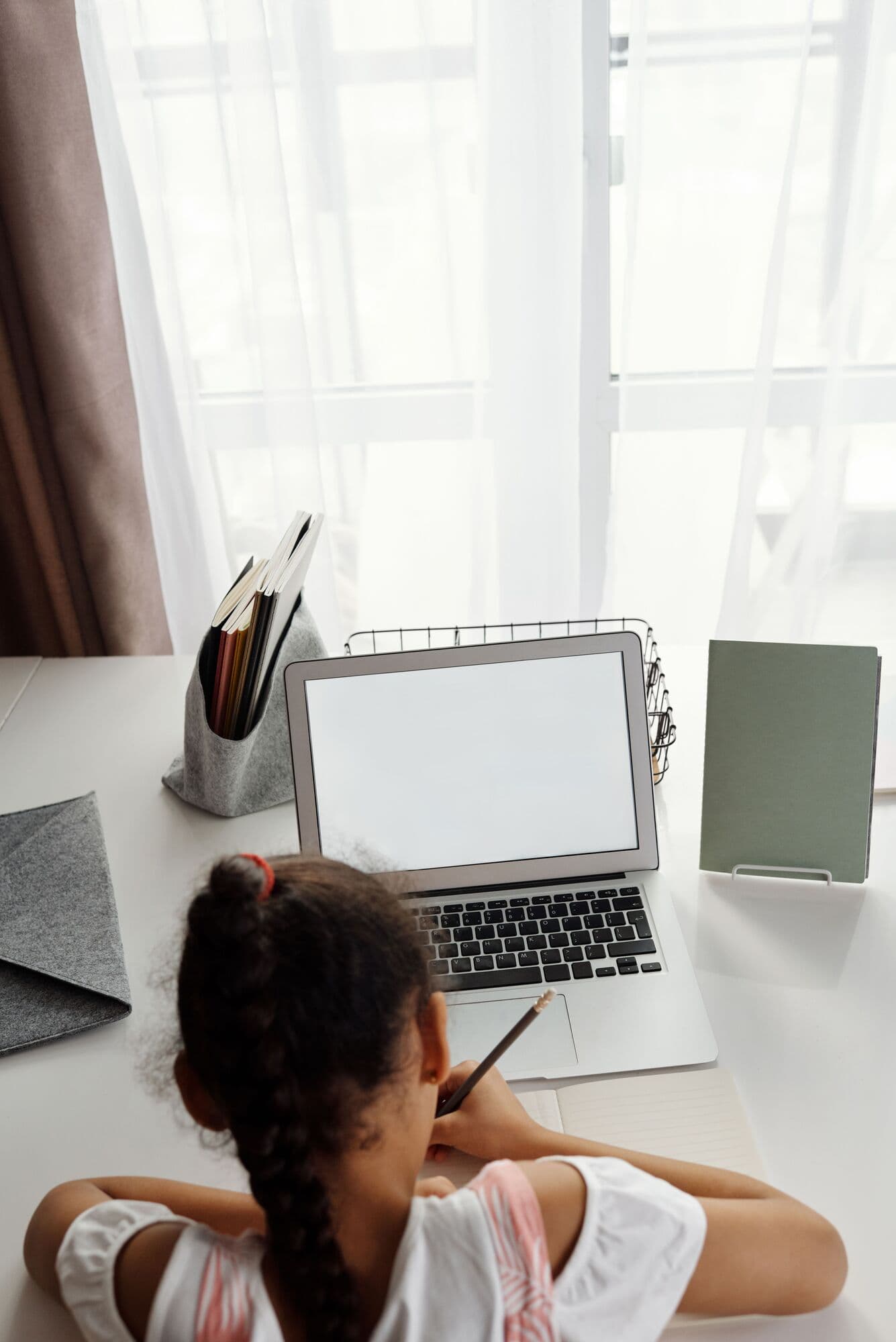 A primary pupil writes beside her laptop